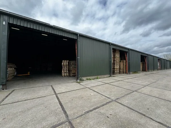 Rij donkere opslagloodsen aan de Graaf van Lynden van Sandenburgweg met stapels houten pallets bij de open ingangen.